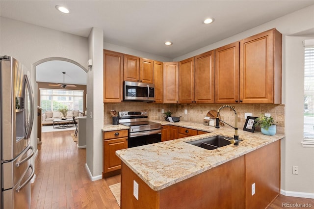 kitchen with appliances with stainless steel finishes, a sink, light stone counters, a peninsula, and backsplash