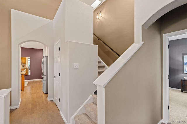 stairs featuring arched walkways, wood finished floors, and baseboards