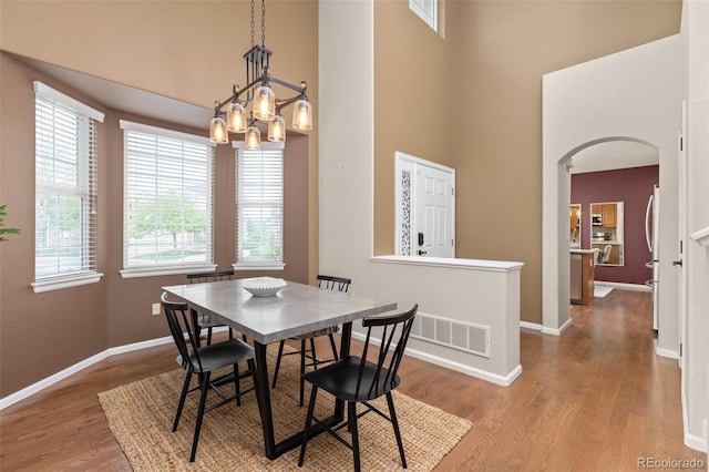 dining area featuring a high ceiling, arched walkways, wood finished floors, a chandelier, and baseboards