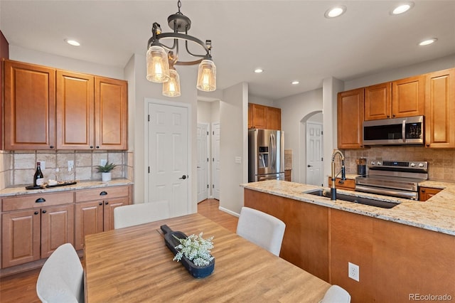 kitchen with appliances with stainless steel finishes, a sink, recessed lighting, arched walkways, and light stone countertops