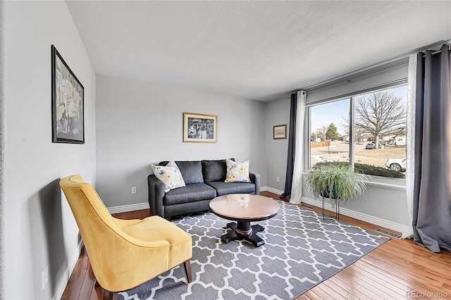 living room with visible vents, a textured ceiling, baseboards, and wood-type flooring