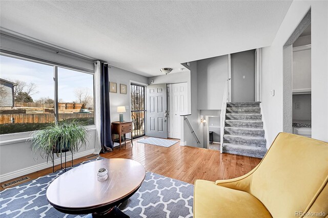 living room featuring visible vents, baseboards, stairs, wood finished floors, and a textured ceiling