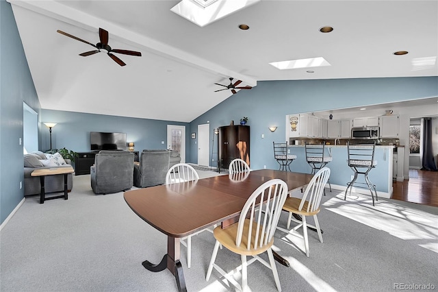 carpeted dining room with baseboards, lofted ceiling with skylight, and ceiling fan