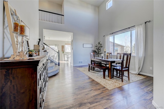 dining room with visible vents, stairway, a high ceiling, wood finished floors, and baseboards