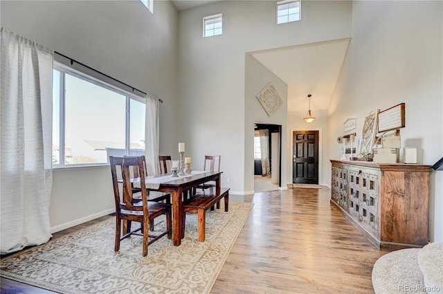 dining area with light wood-type flooring, a high ceiling, and baseboards
