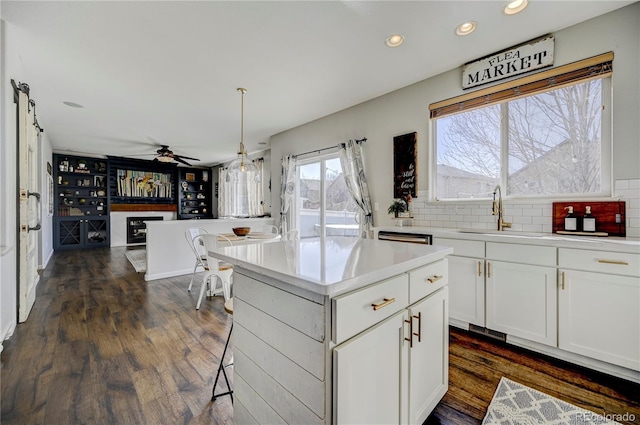 kitchen featuring light countertops, backsplash, white cabinetry, a ceiling fan, and a sink