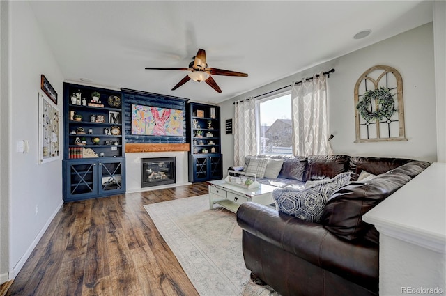 living room with ceiling fan, a glass covered fireplace, wood finished floors, and baseboards