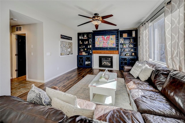 living room with a glass covered fireplace, baseboards, visible vents, ceiling fan, and wood finished floors