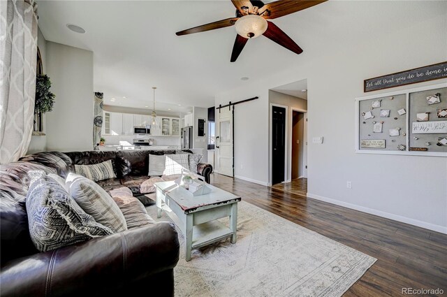 living room with baseboards, a ceiling fan, a barn door, and wood finished floors