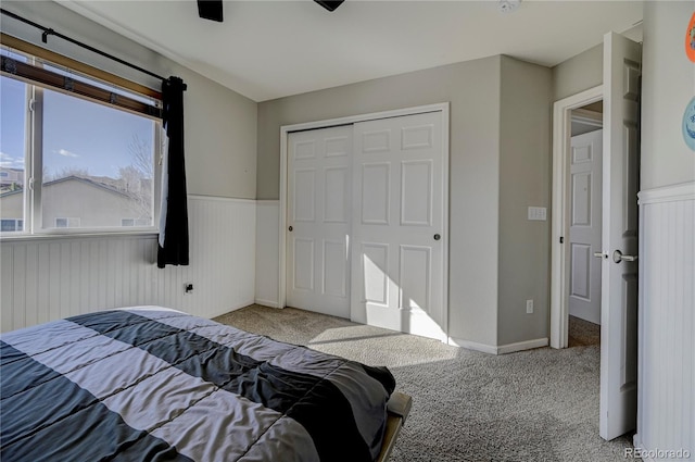 bedroom featuring carpet floors, a wainscoted wall, a ceiling fan, and a closet