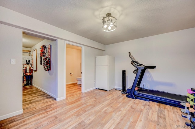 workout area featuring baseboards, light wood finished floors, and a textured ceiling