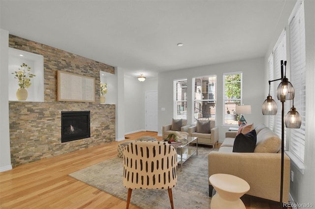 living room featuring wood finished floors, a stone fireplace, and baseboards