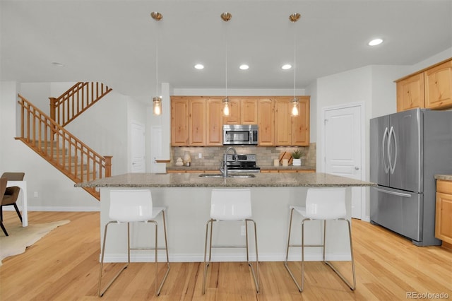 kitchen featuring appliances with stainless steel finishes, a sink, a breakfast bar area, light wood-style flooring, and recessed lighting