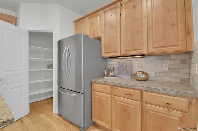 kitchen featuring freestanding refrigerator, light brown cabinetry, light wood-style floors, decorative backsplash, and light countertops