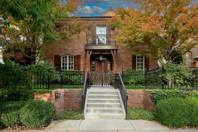 view of front of property with stairs, brick siding, a fenced front yard, and a balcony