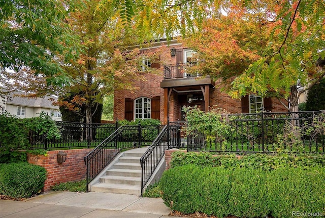 view of front of home with brick siding, stairway, fence, and a balcony