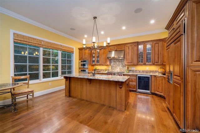 kitchen with wine cooler, an island with sink, glass insert cabinets, and under cabinet range hood