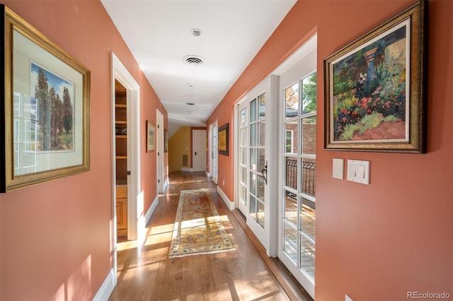 hallway with french doors, light wood-style flooring, visible vents, and baseboards