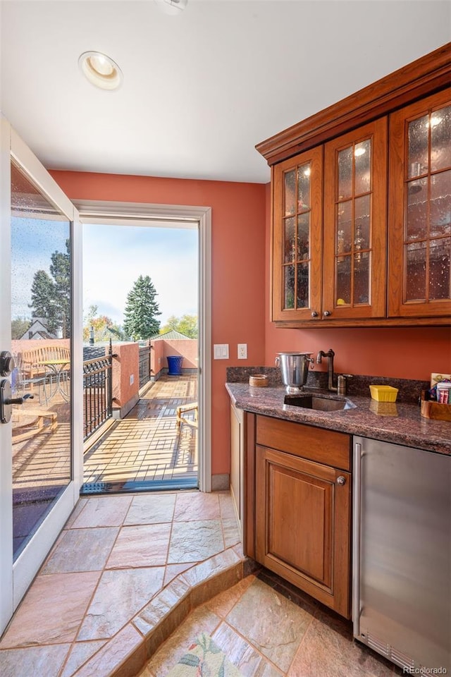 bar featuring stone tile floors, baseboards, a sink, and refrigerator