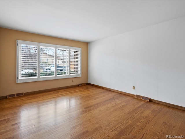 unfurnished room with baseboards, visible vents, and wood finished floors