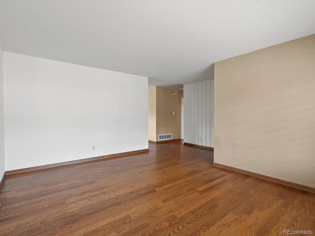 empty room with wood finished floors, visible vents, and baseboards