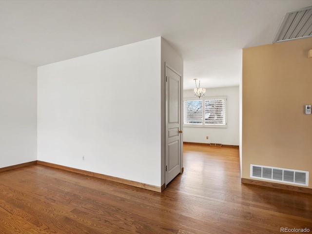 empty room with a notable chandelier, wood finished floors, visible vents, and baseboards