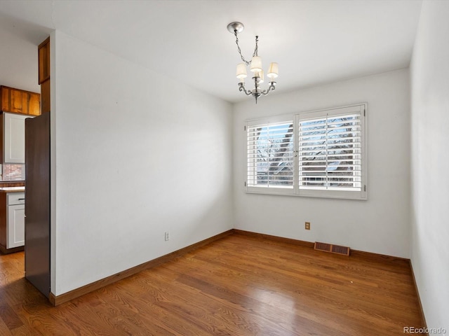 unfurnished dining area featuring a chandelier, wood finished floors, visible vents, and baseboards