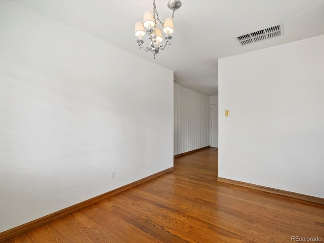 empty room with baseboards, visible vents, a chandelier, and wood finished floors