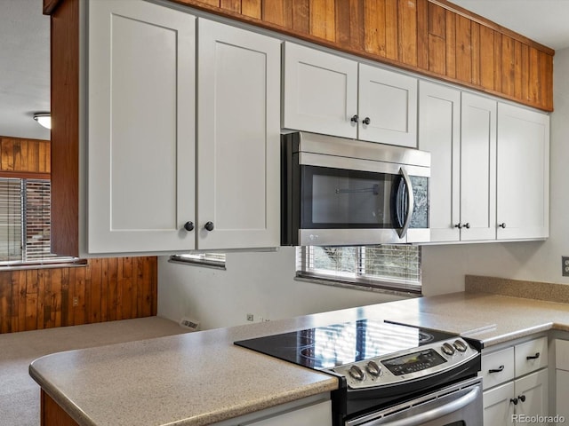 kitchen with appliances with stainless steel finishes, a healthy amount of sunlight, wooden walls, and white cabinetry