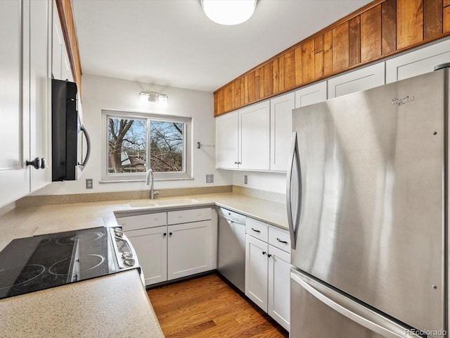 kitchen with light countertops, freestanding refrigerator, white cabinets, a sink, and dishwasher