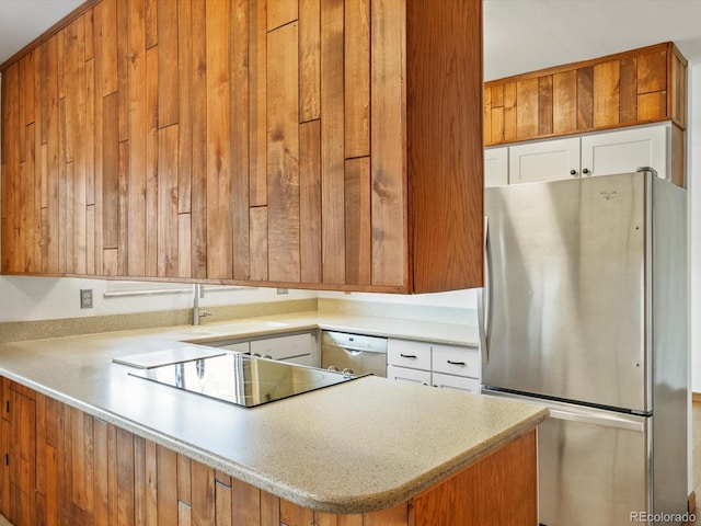 kitchen featuring black electric stovetop, a peninsula, white cabinets, freestanding refrigerator, and dishwasher