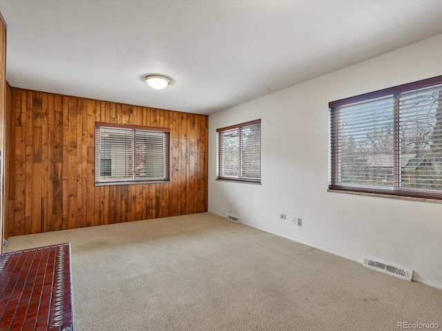 carpeted empty room with visible vents and wood walls