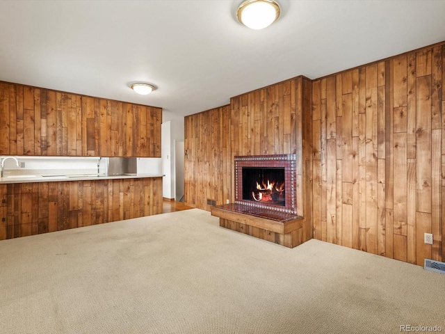 unfurnished living room featuring carpet, wood walls, a brick fireplace, and visible vents