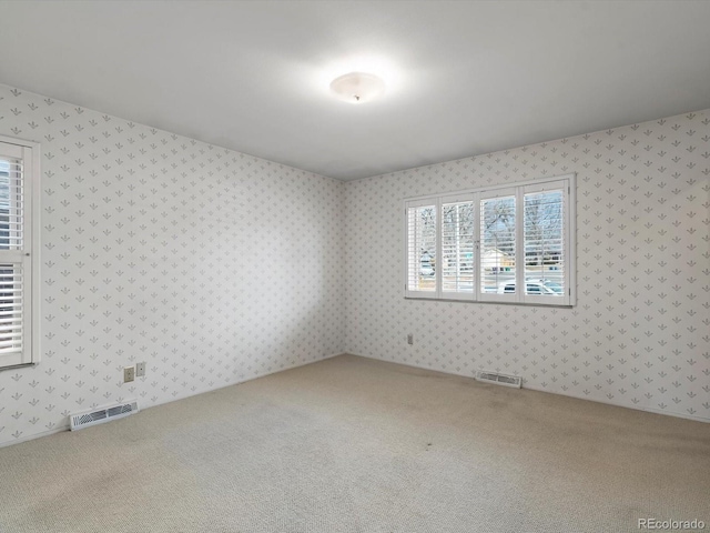 carpeted empty room featuring wallpapered walls and visible vents