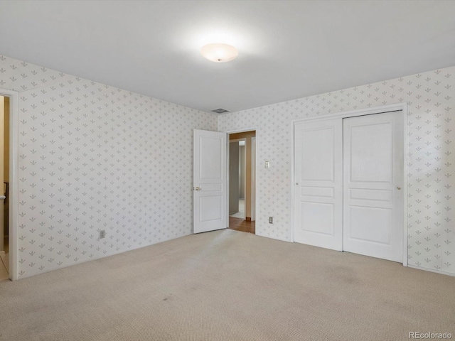 unfurnished bedroom with carpet floors, a closet, visible vents, and wallpapered walls