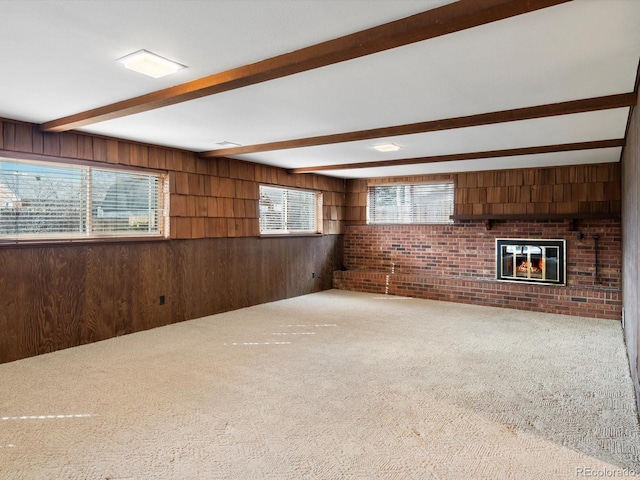 unfurnished living room with carpet floors, beam ceiling, a fireplace, and wood walls