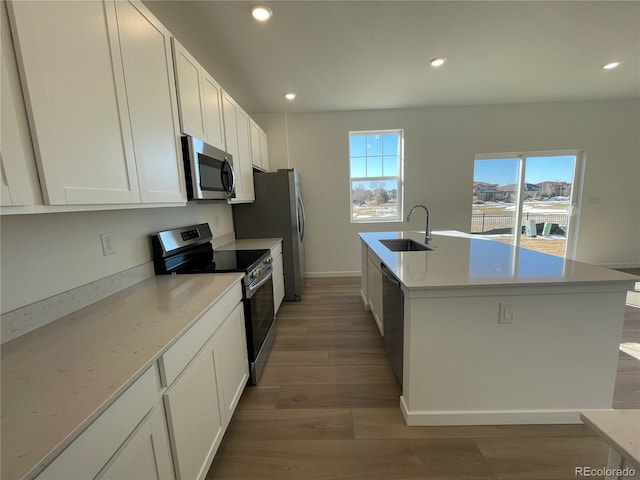 kitchen featuring white cabinetry, wood-type flooring, sink, stainless steel appliances, and a center island with sink