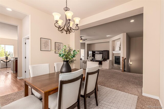 dining space with light carpet, baseboards, recessed lighting, a tiled fireplace, and ceiling fan with notable chandelier