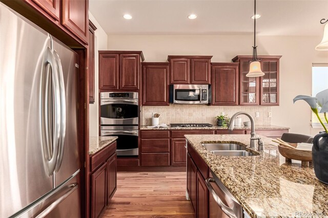 kitchen featuring pendant lighting, light wood-type flooring, a sink, appliances with stainless steel finishes, and backsplash