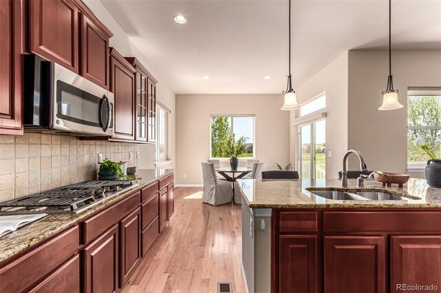 kitchen featuring light stone counters, appliances with stainless steel finishes, a sink, decorative backsplash, and light wood-type flooring