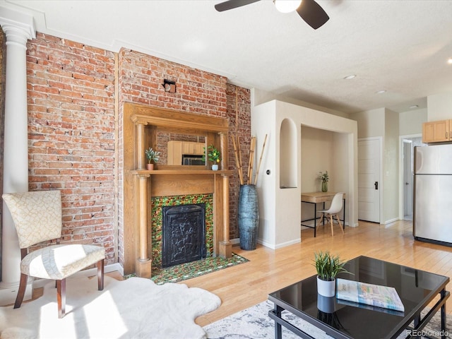 living room with a tiled fireplace, ceiling fan, brick wall, and light wood-type flooring