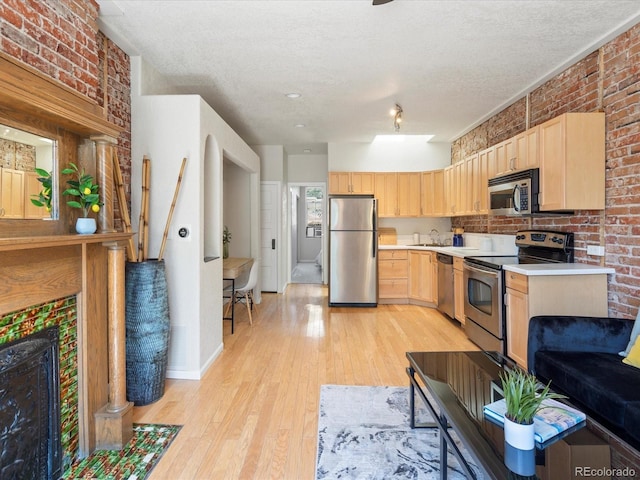 kitchen featuring appliances with stainless steel finishes, light brown cabinetry, brick wall, sink, and light hardwood / wood-style flooring