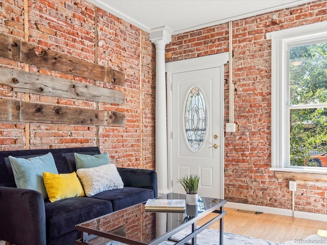 living room featuring hardwood / wood-style floors, ornate columns, crown molding, and brick wall