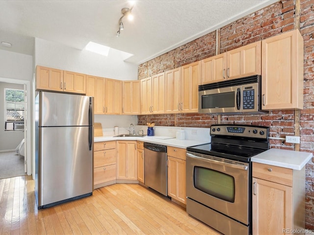 kitchen featuring light brown cabinets, sink, stainless steel appliances, and brick wall