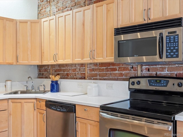 kitchen featuring brick wall, light brown cabinetry, sink, and appliances with stainless steel finishes