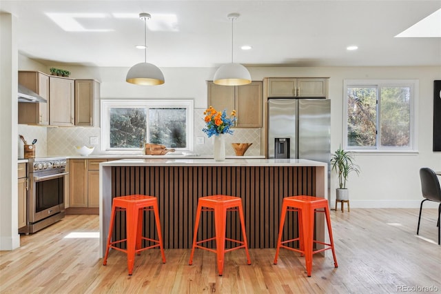 kitchen featuring tasteful backsplash, a center island, light wood-type flooring, appliances with stainless steel finishes, and under cabinet range hood
