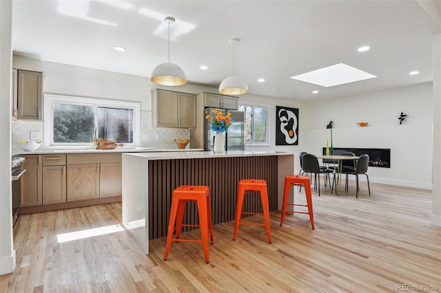 kitchen with a center island, a skylight, backsplash, light wood-style flooring, and stainless steel refrigerator