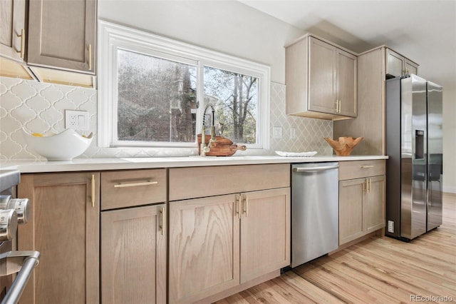 kitchen featuring light countertops, backsplash, appliances with stainless steel finishes, light wood finished floors, and light brown cabinetry
