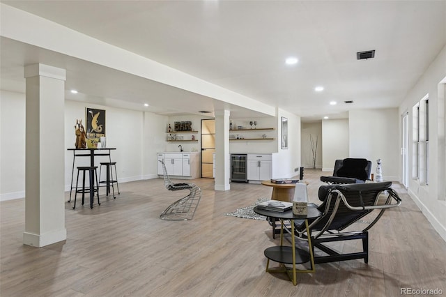 living room featuring wet bar, baseboards, light wood-type flooring, and beverage cooler