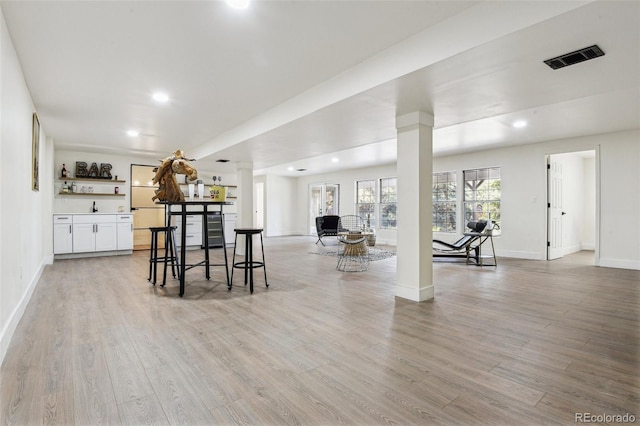 interior space with baseboards, ornate columns, bar area, and light wood-style floors